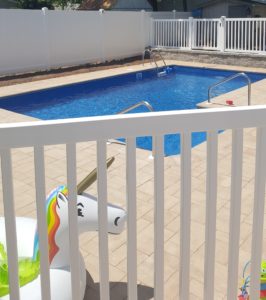 A white vinyl picket fence encloses a pool area with a unicorn pool float in the foreground.
