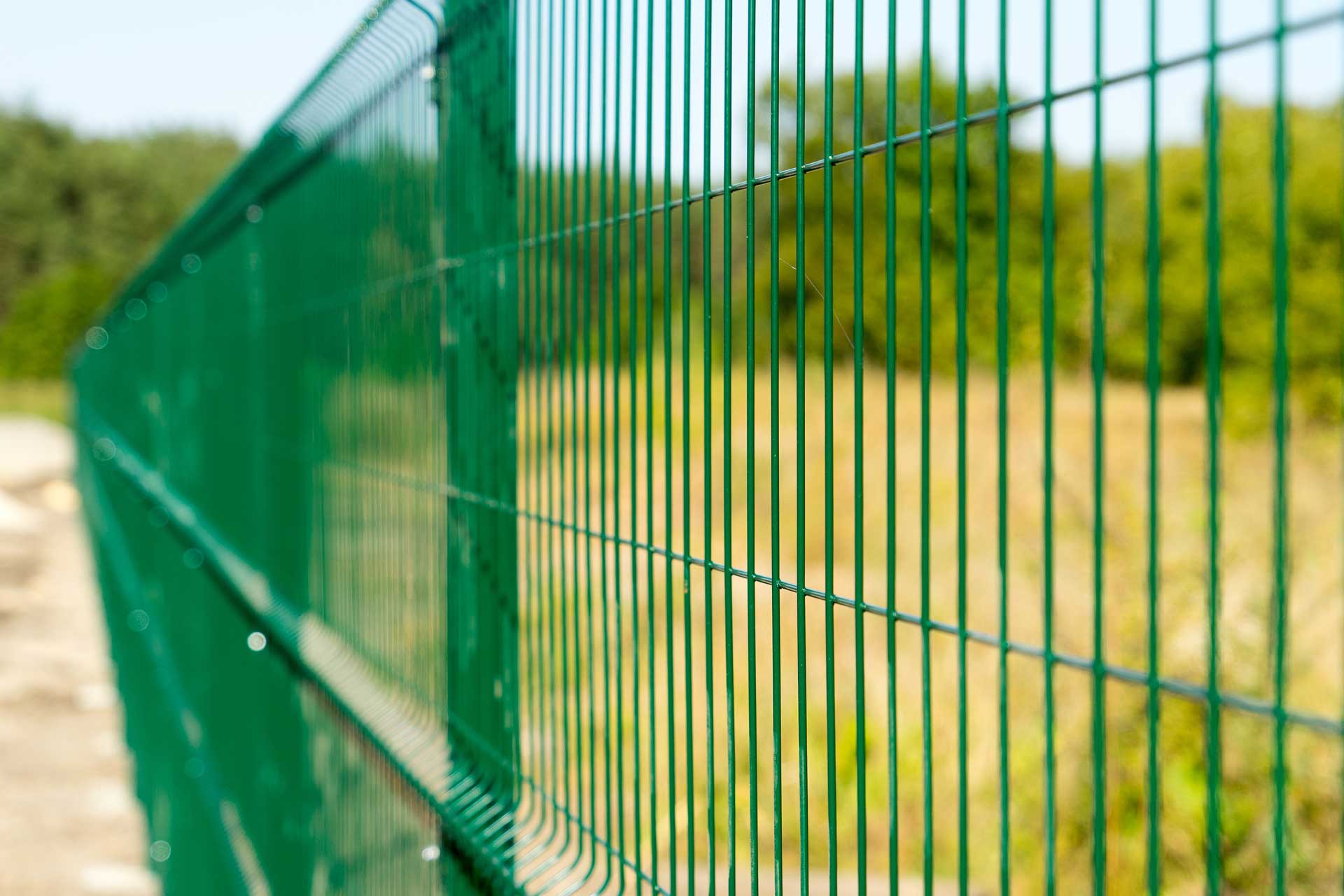 A green welded wire fence is shown up close with an open field in the background.