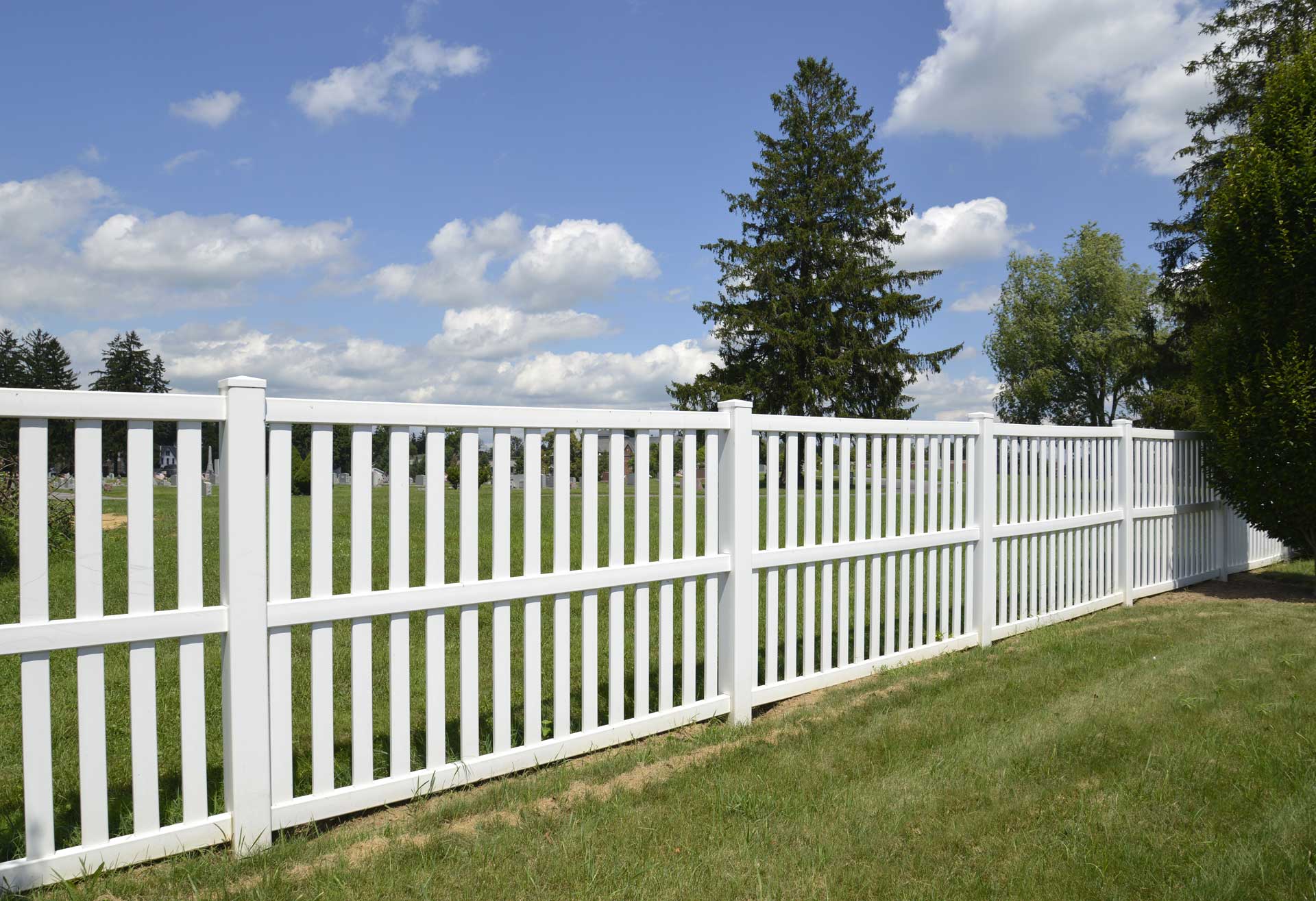 A newly constructed combo style vinyl fence against a bright blue sky and green grass