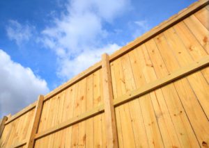A newly constructed solid board wood fence seen from below against a bright blue sky