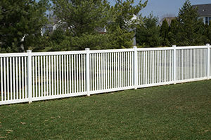 A new white vinyl fence by a grass area with trees behind it.