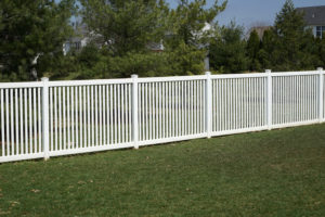 A new white vinyl fence by a grass area with trees behind it.