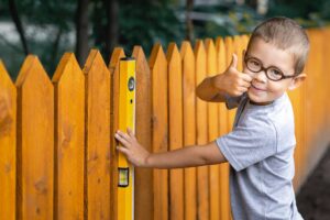 Happy young boy holding a level up against a newly installed wood fence
