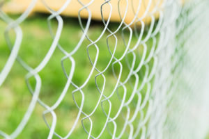 Close up photo of light silver chain link fence against green grass